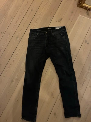 Svarta Replay jeans med stretch - Svarta blåa jeans från Replay i slim fit-modell med lätt tvättade detaljer. Klassisk femficksdesign, normal midja och dragkedjegylf. Tillverkade i stretchigt denimtyg för skön passform och stilren look. Perfekta för dig som gillar en modern och enkel stil.