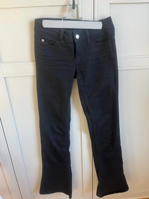 Svarta bootcut jeans Cheap Monday - Säljer ett par svarta bootcut jeans från Cheap Monday med klassisk femficksmodell och en cool rosa logga bak i midjan. Jeansen har normal midja och är tillverkade i stretchigt material för skön passform. Andvända endast en gång i strl 25/32 