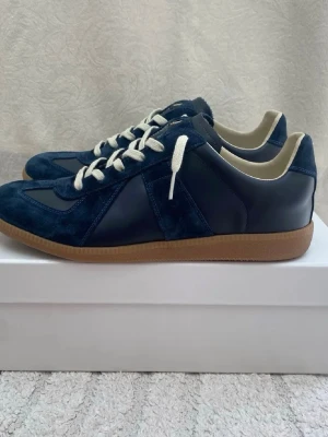 Blå sneakers i mocka och läder - Snygga sneakers i djupblå mocka och slätt läder med vita skosnören och klassisk gummisula. Skorna har en retroinspirerad siluett och beige innerfoder för extra komfort. Perfekta för dig som gillar stilrena och tidlösa sneakers.