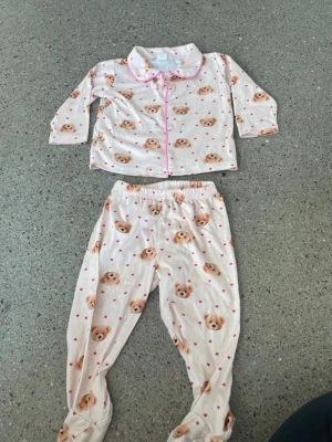Söt pyjamas med nalletryck från SHEIN - Supersöt tvådelad pyjamas från SHEIN i ljusrosa med gulliga nalletryck och små rosa hjärtan. Setet har långärmad skjorta med rosa kantband och matchande byxor med resår i midjan. Perfekt för mysiga kvällar hemma.