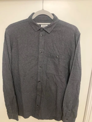 Mörkgrå skjorta från Weekday herr storlek S - Stilren mörkgrå skjorta från Weekday med klassisk krage och knappstängning framtill. Skjortan har en bröstficka med knapp och är tillverkad i mjuk bomull. Perfekt för dig som gillar en enkel och clean look. Mycket bra skick, herr storlek S.