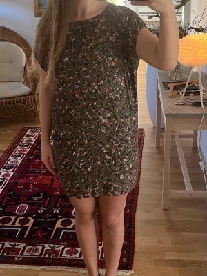 Kortklänning  - Säljer en söt kortklänning med fint mönster i gröna och rosa toner. Klänningen har rund hals, korta ärmar och en avslappnad passform. Perfekt för varma dagar och enkel att styla med sneakers eller sandaler.