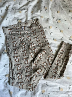 Beige leggings med rådjurstryck barn st 122/128 - Säljer ett par beige leggings med gulligt rådjurstryck över hela plagget. Mjukt och stretchigt material som passar perfekt för en avslappnad stil. Resår i midjan för extra komfort. Storlek 128, passar ca 7-8 år.