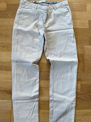Beige chinos - Snygga beige chinos med rak passform och klassiska fickor fram och bak. Tillverkade i ett mjukt bomullstyg som känns skönt mot huden. Perfekta för en clean och stilren look. Bälteshällor i midjan och diskreta sömmar för en enkel vibe.
