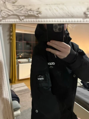 Svart vindjacka från Dope - Snygg svart vindjacka från Dope med huva och vita detaljer. Jackan har logga på bröstet och ärmen samt praktiska fickor. Perfekt för blåsiga dagar och outdoor-aktiviteter. Materialet är slitstarkt och vattenavvisande.