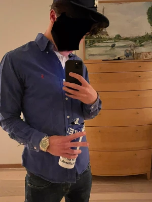 Blå skjorta från Polo Ralph Lauren - Klassisk blå skjorta från Polo Ralph Lauren med röd broderad logga på bröstet. Skjortan har lång ärm, knappar framtill och en tidlös passform. I storlek Small. Perfekt till sommaren och vid speciella tillfällen 🤩🤩