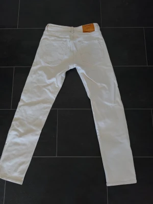 Vita jeans från Jack & Jones - Snygga vita jeans från Jack & Jones med klassisk femficksdesign och raka ben. Jeansen har en läderpatch med logga bak i midjan och är tillverkade i ett mjukt bomullsmaterial. Perfekta för dig som vill ha en clean och stilren look.