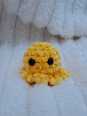 Liten gul virkad bläckfisk med nyckelring - Liten handgjord bläckfisk i gult chenillegarn med nyckelring. Bläckfisken har även sitt egna namn som sitter på produkten vid köp. Produkten passar perfekt som dekoration på väskan eller nyckelknippa. Färgerna på bilden kan vara lite annorlunda i verkligheten. Eftersom produkten innehåller säkerhetsögon rekommenderas den inte för barn under 3 år. 
