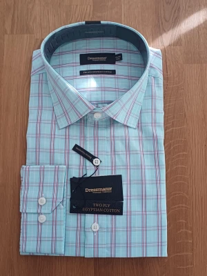 Rutig skjorta Dressmann bomull - Snygg rutig skjorta från Dressmann i ljusblått med röda och vita ränder. Tillverkad av tvålagers egyptisk bomull för extra komfort. Klassisk krage, långärmad och med vita knappar framtill. Perfekt för en clean och fräsch look.