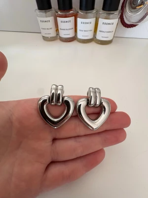 Silvriga hjärtörhängen ifrån Edblad - Säljer ett par chunky örhängen i blankt silverfärgat metallmaterial. Örhängena har en öppen hjärtformad design och breda fästen upptill.