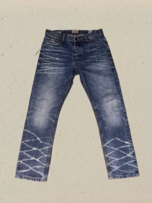 Vintage Jack&Jones jeans - Säljer ett par blå vintage jack&jones jeans med raka ben med slitna detaljer framtill och baktill. Materialet är denim i bomull och färgen är tvättad blå med vita effekter.