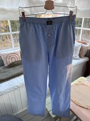 Blårutiga pyjamasbyxor från Polo Ralph Lauren - Säljer ett par klassiska blårutiga pyjamasbyxor från Polo Ralph Lauren. Byxorna har resår i midjan med dragsko, knäppning framtill och sidofickor. Tillverkade i mjuk bomull och har den ikoniska Polo-loggan broderad vid midjan. Dessa byxor är i utmärkt skick förutom den lilla defekten på häger ficka. Vi har själva lappat defekten. Utöver pyjamas, fungerar dessa utmärkt som sommarbyxor. Skick: 9.5/10 (ej 10/10 pga den lilla defekten). Storlek: 170cm (S-M). Pris: 300sek. Nypris ca. 800 sek. 