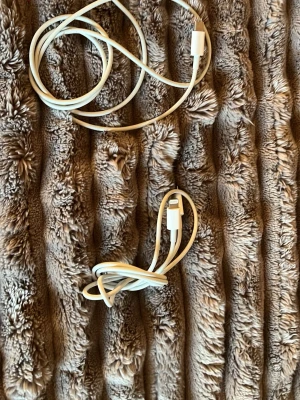 Två vita laddkablar till iPhone - Säljer två vita laddkablar för mobiltelefon. Ena kabeln har USB-C kontakt och den andra har Lightning-kontakt, båda i klassisk vit färg och tillverkade i plast. Perfekt för laddning och dataöverföring till olika mobiler och tillbehör.