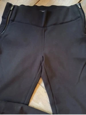 Svarta leggings med dragkedjor - Säljer ett par svarta leggings med snygga dragkedjor vid sidorna. De har en tight passform och är tillverkade i ett stretchigt material som sitter snyggt på benen. Från butiken Zara, mått midja 35x2, gren 22 cm. Storlek L men upplever dem som S. Oanvända. Mörkt blåa.