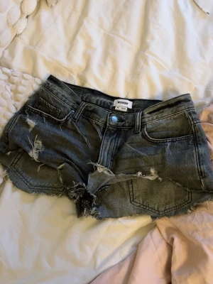 Grå slitna jeansshorts Weekday - Säljer ett par grå jeansshorts från Weekday med råa kanter och slitna detaljer. Shortsen har fem fickor, bälteshällor och knappgylf. Perfekta för en avslappnad och trendig look.