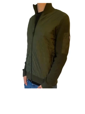 Grön cardiganjacka från J.Lindeberg - Mörkgrön cardiganjacka från J.Lindeberg med stickade ärmar och rygg samt quiltad front. Jackan har hög krage, dragkedja framtill och en patch på ärmen. Perfekt för lager-på-lager och snygg till jeans. Ena fickans dragkedja är fast därför priset. Storlek S