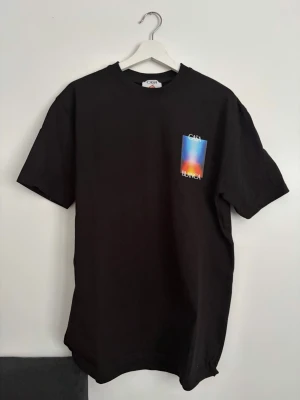 Svart Casablanca t-shirt med tryck - Säljer en svart t-shirt från Casablanca med färgstarkt grafiskt tryck på bröstet och ryggen. T-shirten har normal passform, rund hals och korta ärmar. Materialet är mjuk bomull och trycket har blå, orange och gul ton. Perfekt för dig som gillar streetwear vibes.