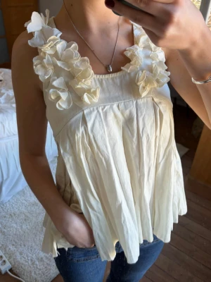 Vit blommig linnetopp med volang - Supersöt vit linnetopp med stora blommor på axelbanden och volangig