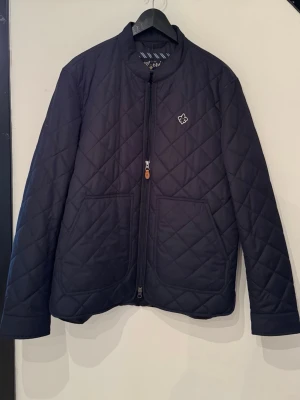 Marinblå jacka från Morris - Stilren marinblå jacka från Morris med rundad krage, dragkedja framtill och två stora fickor. Jackan har ett diskret Morris-emblem på bröstet och är perfekt för höst och vår. Tillverkad i polyester och har långärmad passform. Helt oanvänd med tagg, nypris runt 2500