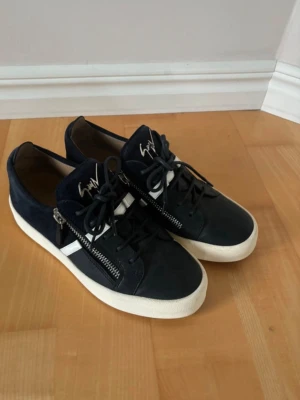 Giuseppe Zanotti skor - Snygga svarta sneakers från Giuseppe Zanotti med vita detaljer och grov vit sula. Skorna har dragkedjor på sidorna, mocka- och läderpaneler samt logga på plösen. Perfekta för dig som vill ha en stilren men ändå unik look. Säljer skorna för att dem är försmå om du har mågrq frågor e det ba o höra av dig