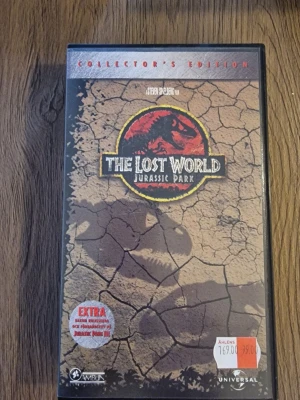 The Lost World Jurassic Park VHS - Collector's Edition av The Lost World: Jurassic Park på VHS. Omslaget är brunt med sprucken jord och den ikoniska dinosaurieloggan i rött och gult. Extra material om Jurassic Park III ingår. Plastfodral med färgtryck och svensk text. Perfekt för samlare av filmklassiker.