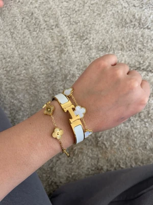 Vitt och guldigt armband med två st fyrklöver armband - Snyggt armband  vitt och guld. Armbandet har den klassiska H-detaljen i rostfritt stål. Perfekt accessoar för att lyfta din outfit med en lyxig touch. H armband 16cm och fyrklöver 17+5cm