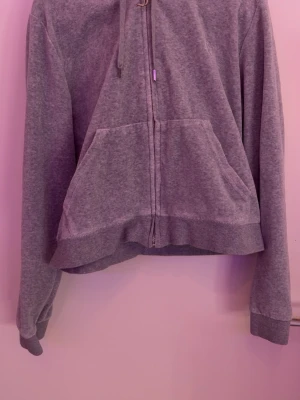 Grå zip hoodie från Juicy Couture - Mysig grå hoodie från Juicy Couture i storlek XL passar L. Tröjan har dragkedja framtill, stor ficka på magen och justerbar huva med snören. Perfekt för en chill och avslappnad stil. Tillverkad i mjukt material som känns skönt mot huden. 