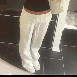 Vita alobha label linne byxor men band - Säljer ett par vita linnebyxor med avslappnad passform och dragsko i midjan. Byxorna har raka ben och är perfekta för en chill och stilren look. Materialet är svalt och luftigt linne, vilket gör dem sköna att bära under varma dagar.