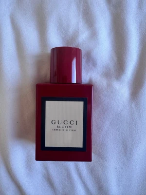 Gucci Bloom Ambrosia di Fiori parfym - Gucci Bloom Ambrosia di Fiori är en elegant parfym i en djup röd, rektangulär flaska med matchande lock. Flaskan har en stilren etikett med svart ram och vit bakgrund. Doften är känd för sina blommiga och intensiva noter, perfekt för dig som vill sticka ut. Helt ny aldrig använd köpte fel 