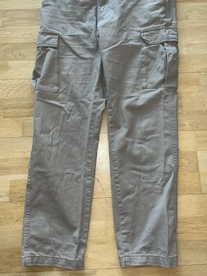 Beige cargobyxor från New Garments - Snygga beige cargobyxor från New Garments med raka ben och stora sidofickor. Tillverkade i ett mjukt bomullstyg med knapp och hällor i midjan. Perfekta för en avslappnad och trendig look.