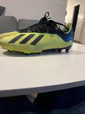 Gula Adidas fotbollsskor med dobbar - Snygga fotbollsskor från Adidas i gul och svart med klassiska tre ränder på sidan. Skorna har snörning, låg profil och dobbar för bra grepp på planen. Ovandelen är tillverkad i ett lätt syntetmaterial som ger bra bollkontroll och komfort .