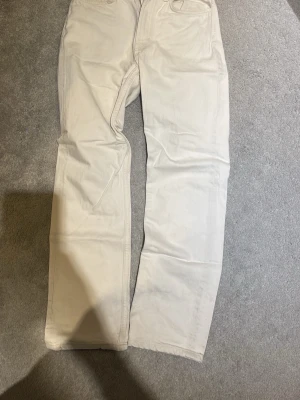 Beiga raka jeans - Säljer ett par beiga jeans med rak passform och klassisk femficksdesign. Jeansen har normal midja och är tillverkade i ett mjukt bomullstyg. Perfekta för en clean och avslappnad stil.