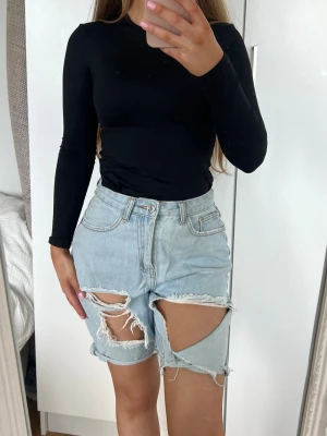 Shorts  - Säljer ett par ljusblå jeansshorts med hög midja och stora slitningar framtill. Shortsen har råa kanter och klassisk knappgylf. Perfekta för en avslappnad och trendig sommarlook. Storlek 36 från Missguided 🩵