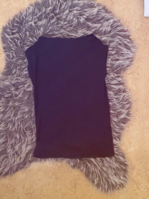 Svart ärmlös topp - En enkel och stilren svart topp utan ärmar. Perfekt att matcha med jeans eller kjol för en clean look. Tunn och mjuk i materialet, med rak passform och rund halsringning.