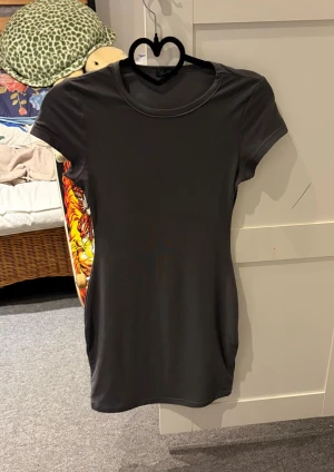 Svart kort klänning från As ever - En enkel och stilren svart kort klänning. Klänningen har rund halsringning och korta ärmar. Passformen är figurnära och materialet känns mjukt och stretchigt, perfekt för en clean och modern look.