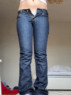 Mörkblå bootcut jeans från Levi's - Säljer ett par mörkblå bootcut jeans från Levi's med klassiska kontrastsömmar och femficksmodell. Jeansen har låg midja och en snygg passform som framhäver benen. Perfekta till sneakers eller boots för en avslappnad look. Midjan rakt över:34cm, Innerben:83cm