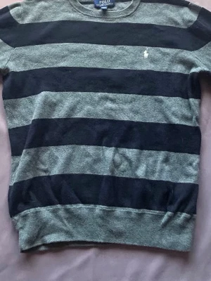 Randig tröja från Polo Ralph Lauren - Mysig långärmad tröja från Polo Ralph Lauren med breda marinblå och grå ränder. Klassisk rund halsringning och diskret broderad logga på bröstet. Perfekt för en avslappnad och stilren look.