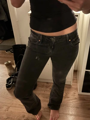 Svarta bootcut jeans med låg midja - Säljer ett par svarta bootcut jeans med låg midja och klassisk femficksmodell. Jeansen har en lätt utsvängd passform nedtill och stängs med knapp och dragkedja. Perfekta för dig som gillar en avslappnad men trendig stil.