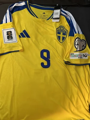 Sverige fotbollströja Isak #9 - Gul och blå  Sverige fotbollströja med nummer 9 och namnet Isak på ryggen. Tröjan har FIFA och UEFA Foundation märken på ärmarna, samt Sveriges landslagsemblem på bröstet. Perfekt för fotbollsfans! Tröjan är ny och har enbart använts vid få tillfällen, storlek L