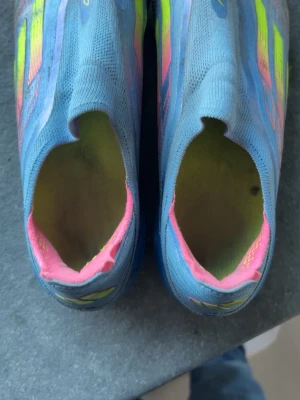 Blå fotbollsskor Adidas f50 - Säljer ett par Adidas f50 elite fotbollsskor i blått med neonrosa och gula detaljer. Skorna har en strömlinjeformad design utan snörning och är tillverkade i syntetmaterial för lätthet och smidighet på planen. Perfekta för dig som vill ha snabbhet och stil.