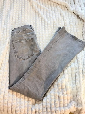 Grå utsvängda jeans från Gina Tricot - Säljer ett par ljusgrå jeans från Gina Tricot med rak passform och klassisk femficksdesign. Jeansen har normal midja och är tillverkade i mjukt denimtyg med lite stretch för extra komfort. Perfekta för en avslappnad och trendig look.