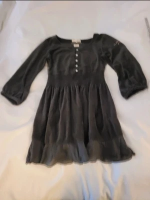 Mörkgrå kort klänning / tunika/topp med knappar - Supersöt mörkgrå topp med trekvartsärm, knappar framtill och volangkant nertill. Smockad midja och dekorativa sömmar på ryggen ger en snygg siluett. Perfekt för dig som gillar en feminin och avslappnad stil.