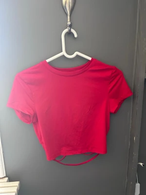 Röd croppad topp med snörning - Snygg röd croppad topp med korta ärmar och rund halsringning. Snörning baktill.