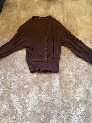 Brun tröja från Gina Tricot - Mysig brun tröja från Gina Tricot med v-ringning och knappar framtill. Koftan har långa ärmar och är fit i midjan. 