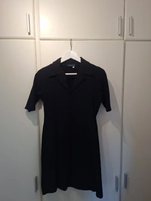 Svart kort klänning från Deep - Stilren kort och figursydd  mörkt marinblå klänning från Deep med krage och tighta ärmar som går nästan ned till armbågen. Figurnära och tidlös design som passar till många olika tillfällen. Tillverkad i ett mjukt jersey med stretch som håller formen bra. Klännijgen ör märkt med storlek L men är mindre. Passar lig som normalt har M.