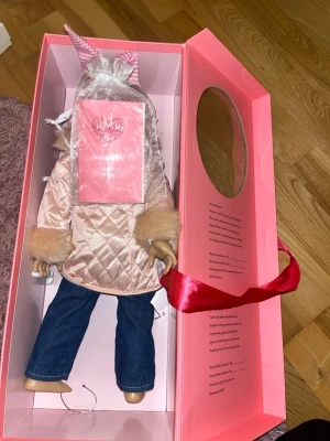 MissMiniMe docka i rosa presentbox - Säljer en MissMiniMe docka i en lyxig rosa presentbox med spegel och röd sidenband. Dockan har blont hår, rosa jacka med fuskpälsdetaljer och blå jeans. Perfekt för dig som gillar samlardockor eller vill ge bort en unik present. KLÄDERNA TILL DOCKAN AÄLJS STYCKVIS!!Dockan kommer med passport boken och i kartongen.