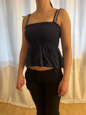 Marinblå topo - En fin marinblå topp som sitter åt åvantill, men är ”volang” pösig nertill. Justerbara axelband som man knyter med tex en rosett. Extremt stretchig, så passar allt mellan xxs och M. Perfekt till sommaren 