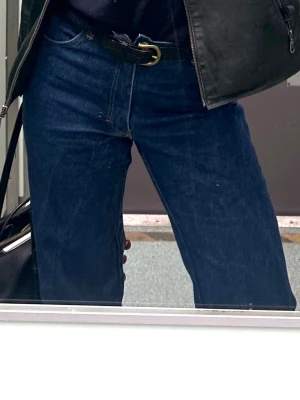 Mörkblå raka jeans med hög midja - Säljer ett par mörkblå jeans med rak passform och hög midja. Klassisk femficksmodell och bälteshällor. Jeansen har en tidlös look och passar perfekt till olika stilar. Materialet är kraftig denim i bomull.