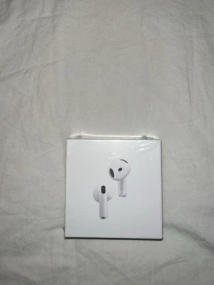 Apple AirPods 4 trådlösa hörlurar - Säljer ett par vita Apple AirPods 4 med stilren design och laddningsetui. Hörlurarna är tillverkade i plast och har en kompakt, ergonomisk form som passar perfekt i öronen. Perfekta för musik, samtal och träning med smidig anslutning till Apple-enheter.
