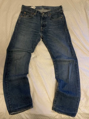 Blå straight jeans från Levi's - Säljer ett par klassiska blå jeans från Levi's med rak passform och fem fickor. Jeansen har slitningar och kontrastsömmar, tillverkade i robust denim. Perfekta för dig som gillar tidlös stil och vill ha ett par jeans som funkar till allt. Storleken är W30 och L32